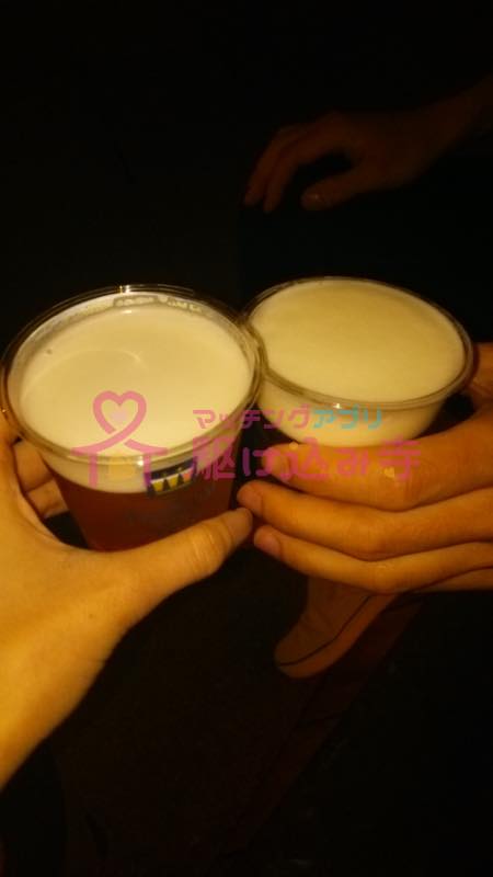 プラスチックの容器に入ったビールで乾杯するカップルの写真