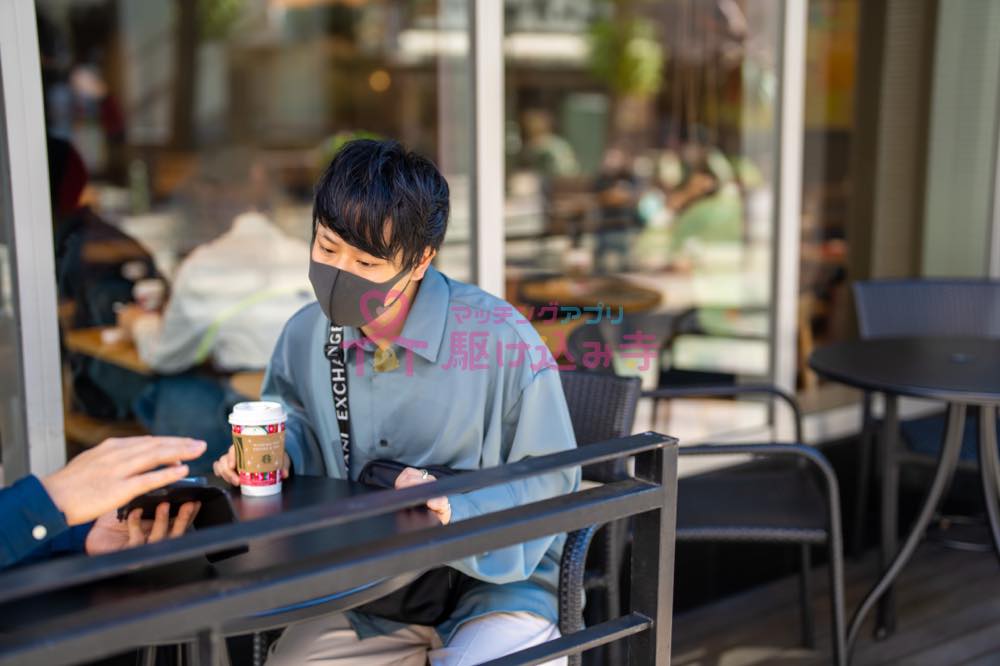 カフェのテラス席でスマホを見る男性